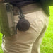 Close-up of a person wearing tactical gear with a small, round black device clipped to their belt, suitable for outdoor or tactical use.